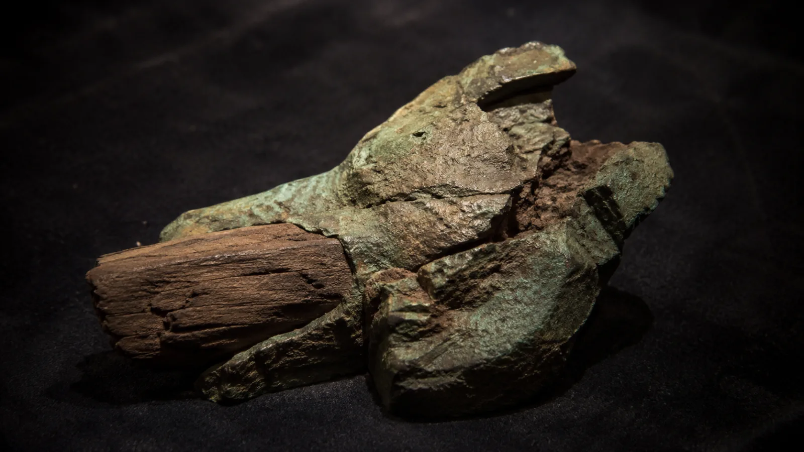 Corroded lump of bronze and wood resting on dark cloth, the object later identified as the Antikythera mechanism